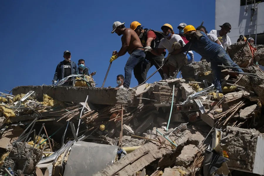 Neighbors and rescue workers clearing rubble on a collapsed slab